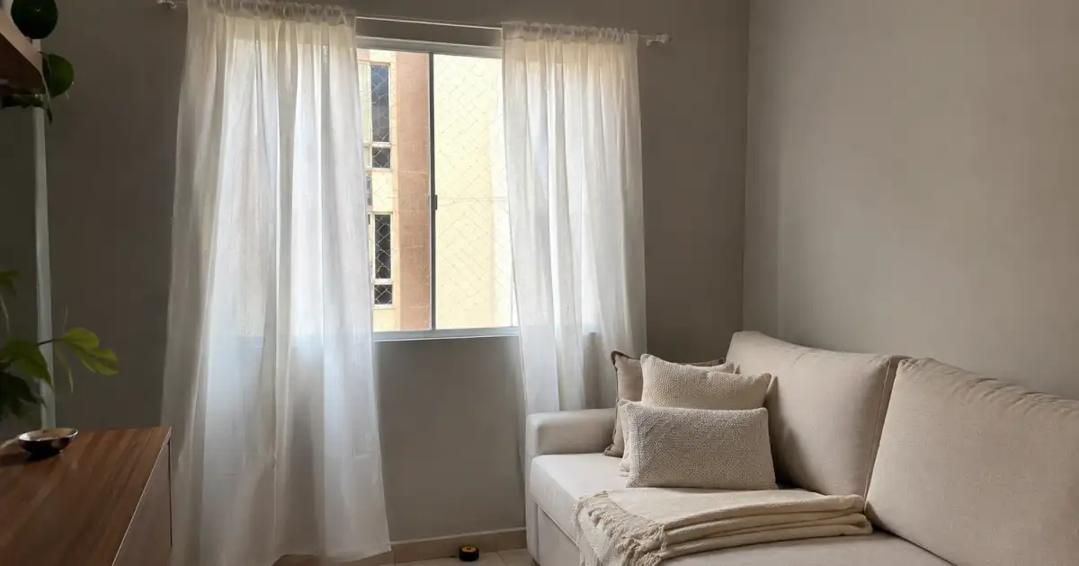 cortina clara sendo medida com trena ao lado de manta e almofadas em apartamento alugado